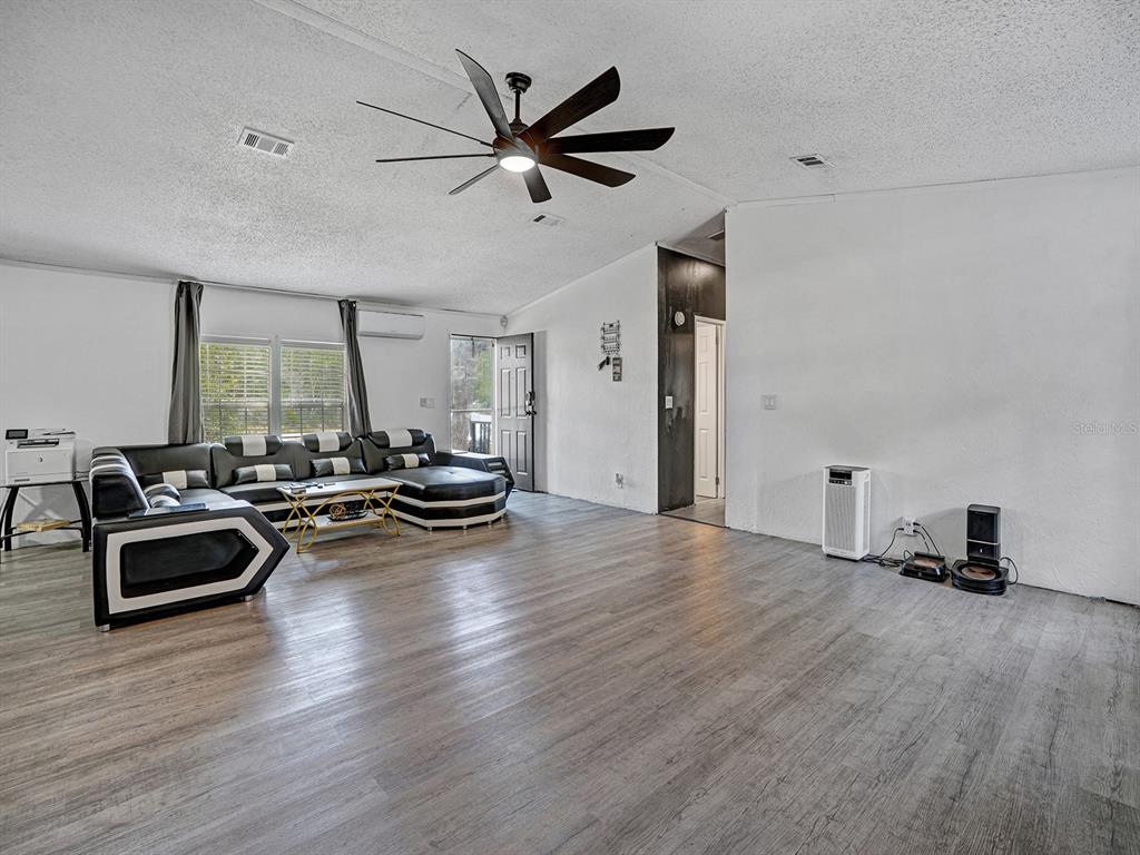 A living room features wood-look flooring, a large sectional sofa, and a ceiling fan — 12845 CASA BIANCA AVENUE, NEW PORT RICHEY, FL
