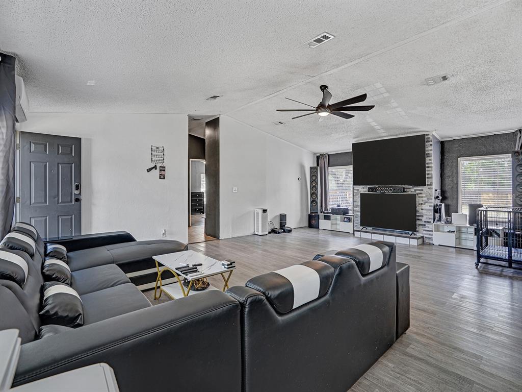 A living room features a large black sectional sofa, a stone fireplace wall, and wood-look flooring — 12845 CASA BIANCA AVENUE, NEW PORT RICHEY, FL