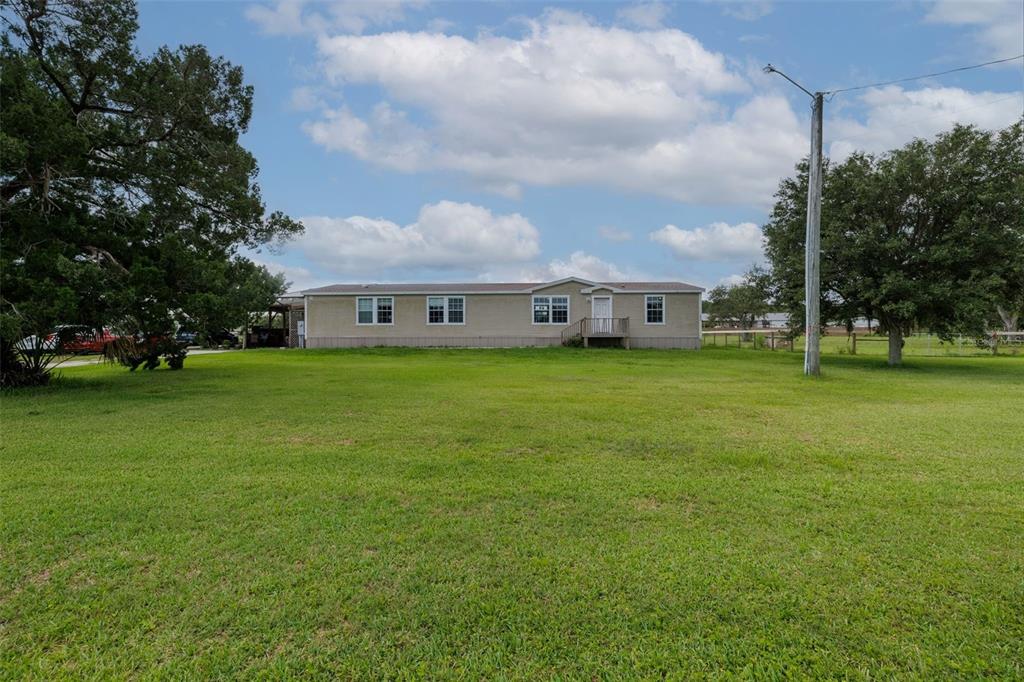 A single-story manufactured home sits on a large, grassy lot under a cloudy sky — 1050 DILLON CIRCLE, NEW SMYRNA BEACH, FL