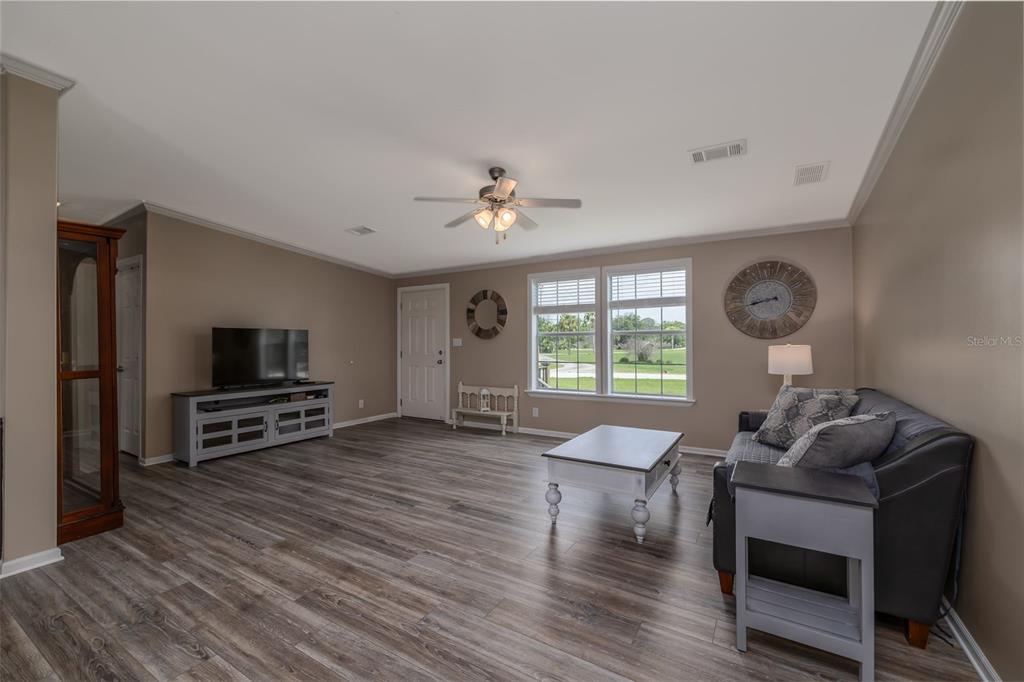A living room features wood-look flooring, a ceiling fan, a sofa, and a television console — 1050 DILLON CIRCLE, NEW SMYRNA BEACH, FL
