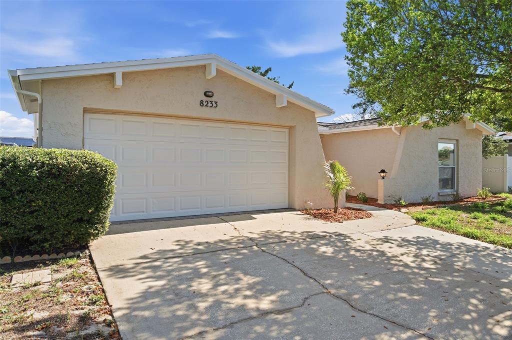 A single-story house with a beige stucco exterior, a two-car garage, and a concrete driveway — 8233 REDFIELD DRIVE, PORT RICHEY, FL