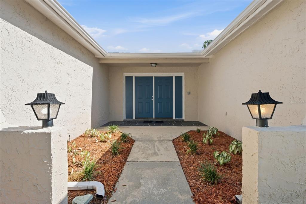 A concrete walkway leads to a blue double front door between two stucco walls — 8233 REDFIELD DRIVE, PORT RICHEY, FL