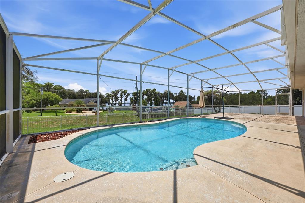 A screened-in patio features a kidney-shaped swimming pool overlooking a grassy yard and lake — 13042 SUNWOOD COURT, CLERMONT, FL