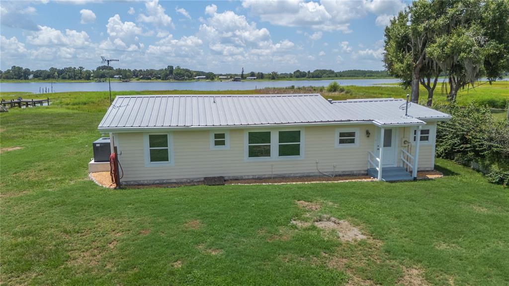 An exterior view of a light yellow, single-story house with a metal roof near water — 5418 COOPER LANE, FORT MEADE, FL