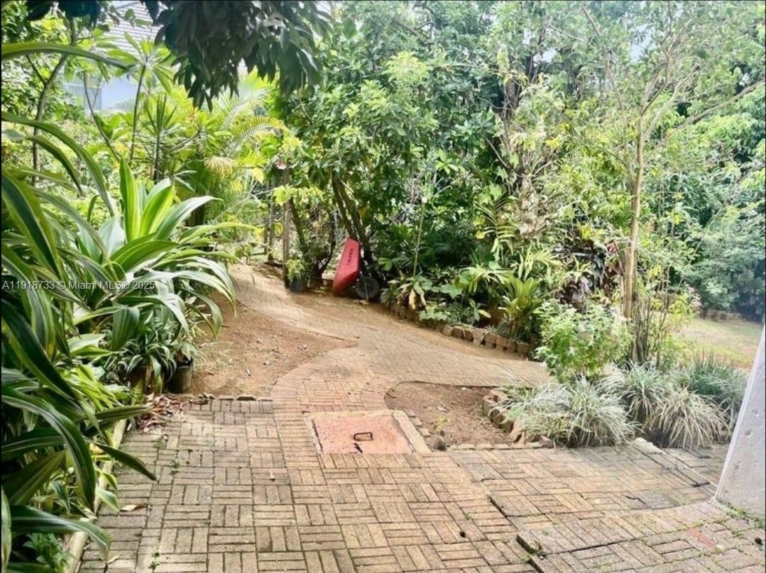 A brick-paved walkway leads through a lush, tree-filled garden area with a red wheelbarrow — 00 WEST PALM GARDENS, BRUMALIA, MANDEVILLE,JAMAICA, NA, NA