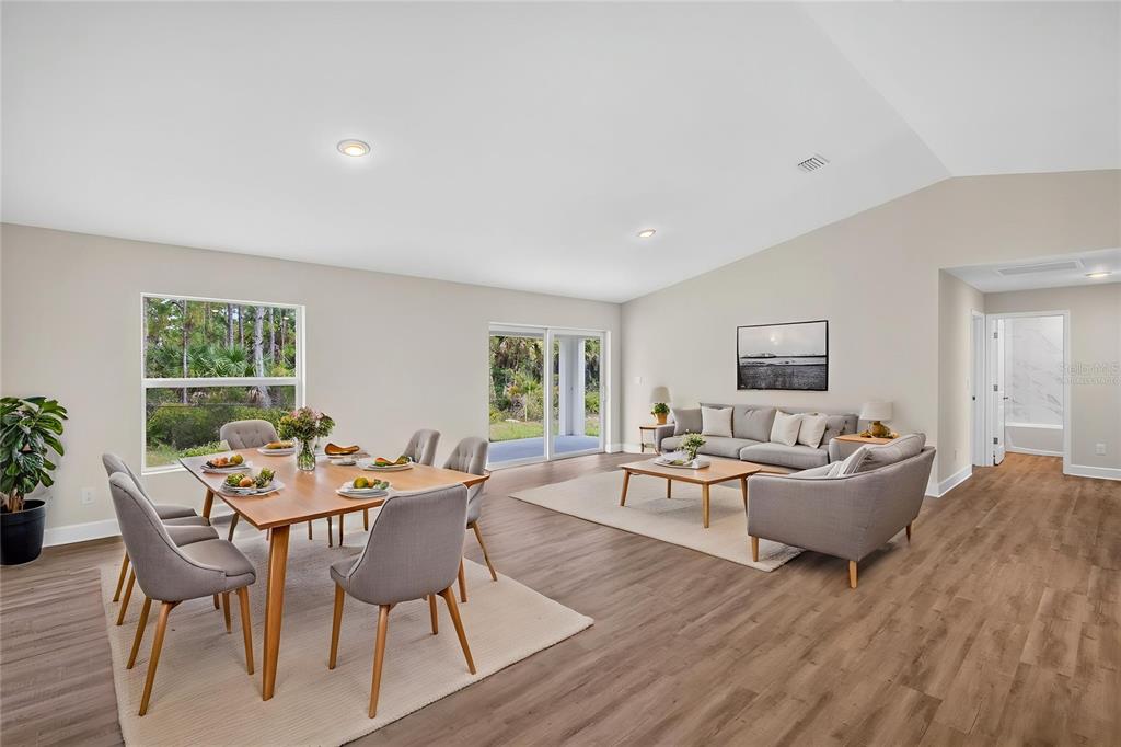 An open-concept living and dining area features light wood flooring and sliding glass patio doors — 23485 BRANCH AVENUE, PORT CHARLOTTE, FL