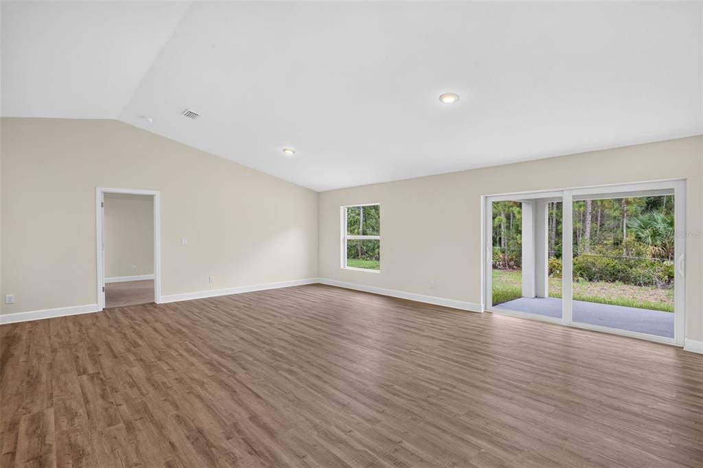 A spacious living room features light walls, wood-look flooring, a vaulted ceiling, and sliding glass doors — 23485 BRANCH AVENUE, PORT CHARLOTTE, FL