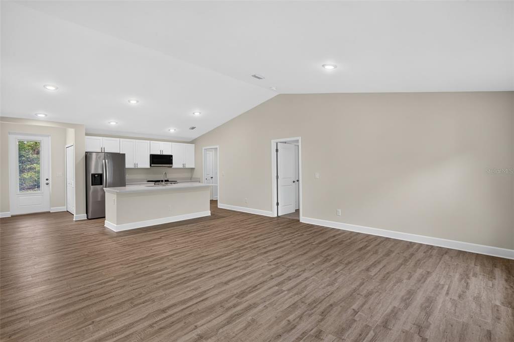 An open-concept kitchen and living area featuring white cabinets, stainless steel appliances, and wood-look flooring — 23485 BRANCH AVENUE, PORT CHARLOTTE, FL