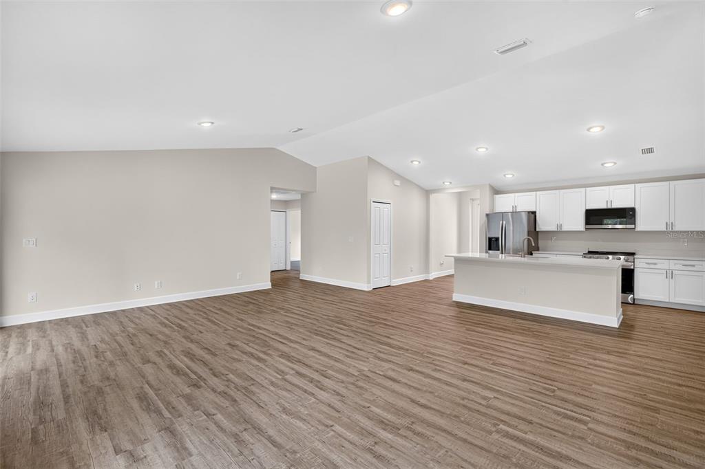 An open-concept living area features light-colored walls, wood-look flooring, and a kitchen with white cabinetry — 23485 BRANCH AVENUE, PORT CHARLOTTE, FL