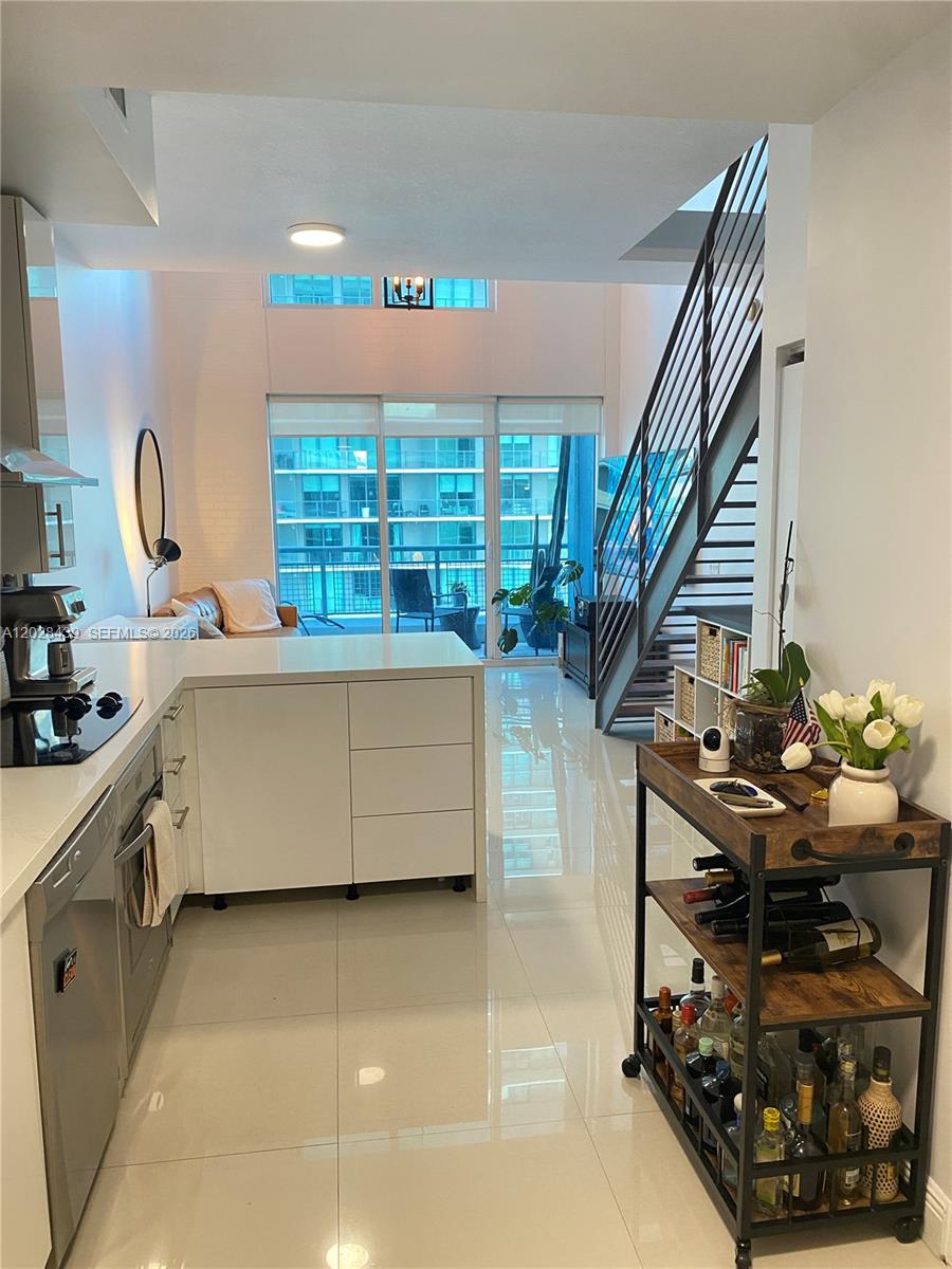 A modern kitchen with white cabinetry and an island opens into a living area — 60 SW 13th St # 2212, Miami FL 33130, MIAMI, FL