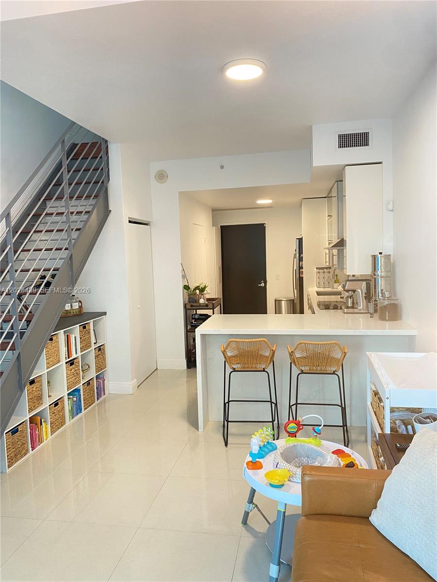 This open-concept kitchen and living area features a staircase, white cabinetry, and a breakfast bar — 60 SW 13th St # 2212, Miami FL 33130, MIAMI, FL