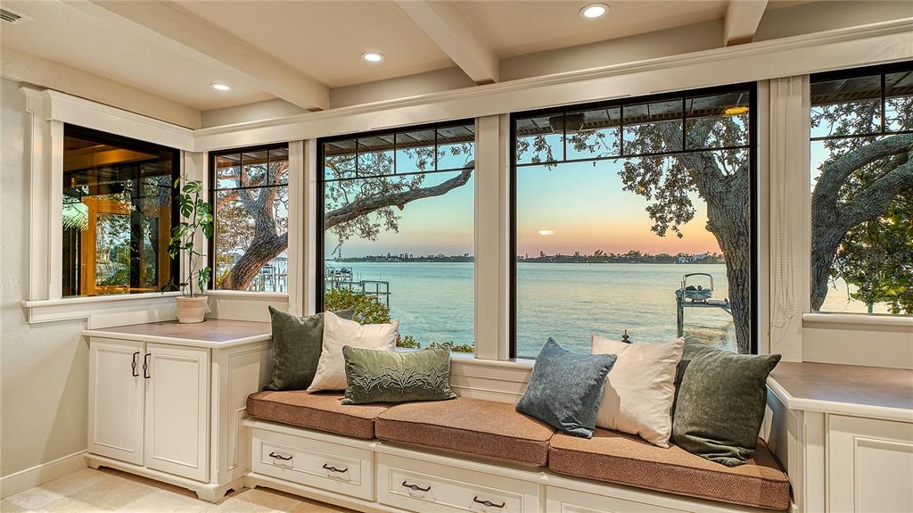 A sunroom with built-in bench seating, storage cabinets, and large windows overlooking a waterfront view — 421 WATERSIDE LANE, NOKOMIS, FL