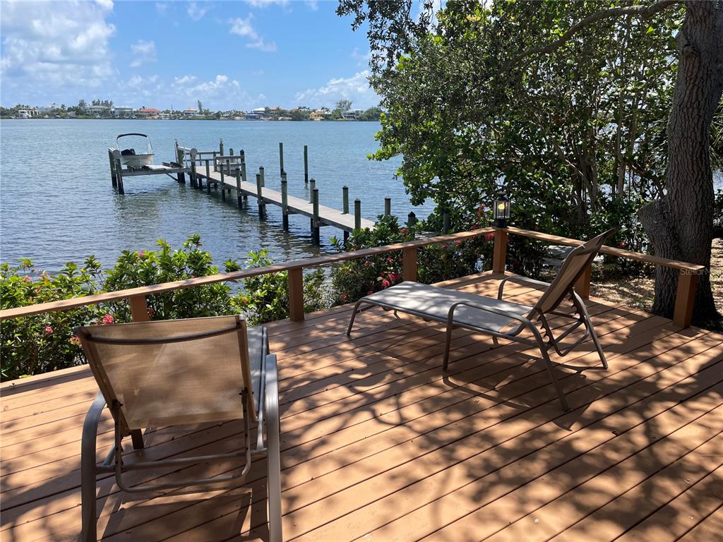 A wooden deck features two lounge chairs overlooking a dock and a calm body of water — 421 WATERSIDE LANE, NOKOMIS, FL