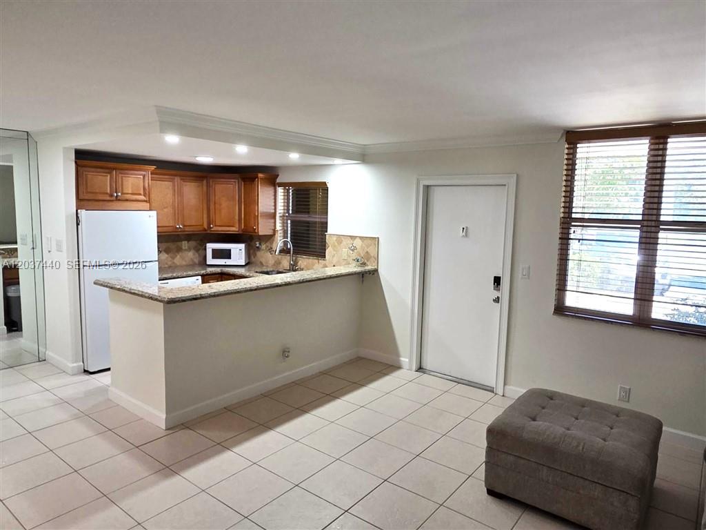 A kitchen with wood cabinets and a granite breakfast bar opens to a tiled room — 2400 NE 10th St # 104, Pompano Beach FL 33062, POMPANO BEACH, FL