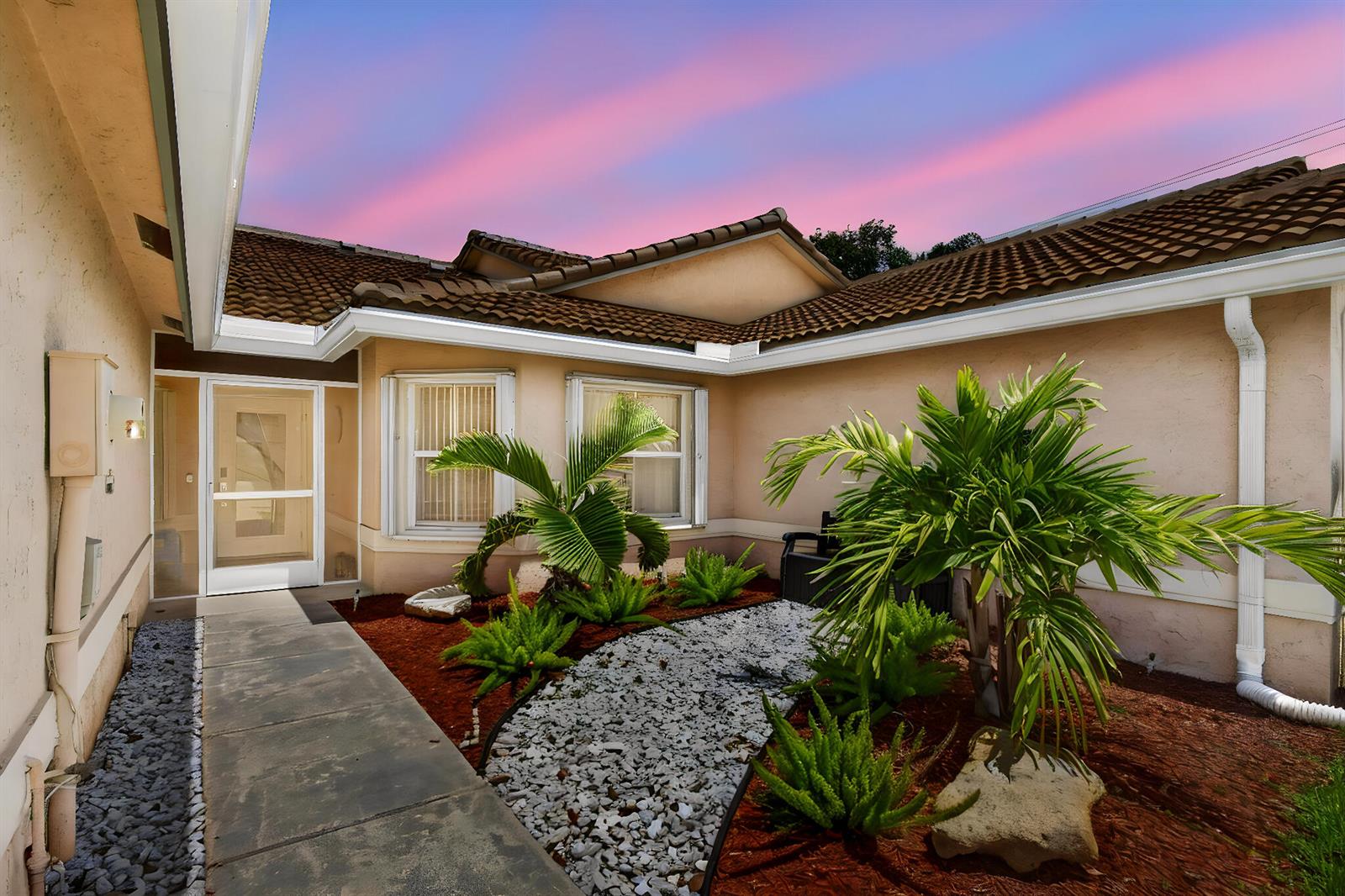 A concrete walkway leads to the front entrance of a house with a landscaped courtyard — 10469 Pelican Drive, Wellington FL 33414, WELLINGTON, FL