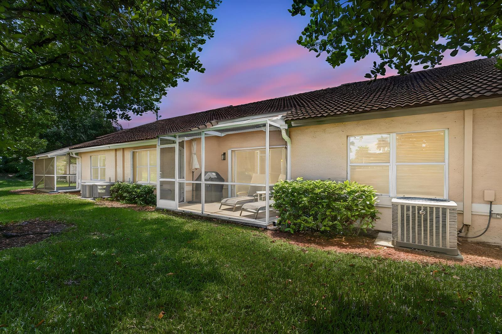 The exterior of a beige house features a screened-in patio and two air conditioning units — 10469 Pelican Drive, Wellington FL 33414, WELLINGTON, FL