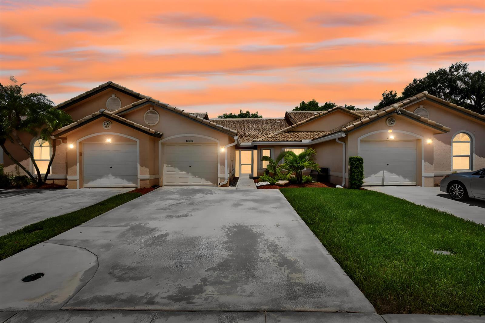 A tan single-story house with three garage doors and a concrete driveway at sunset — 10469 Pelican Drive, Wellington FL 33414, WELLINGTON, FL