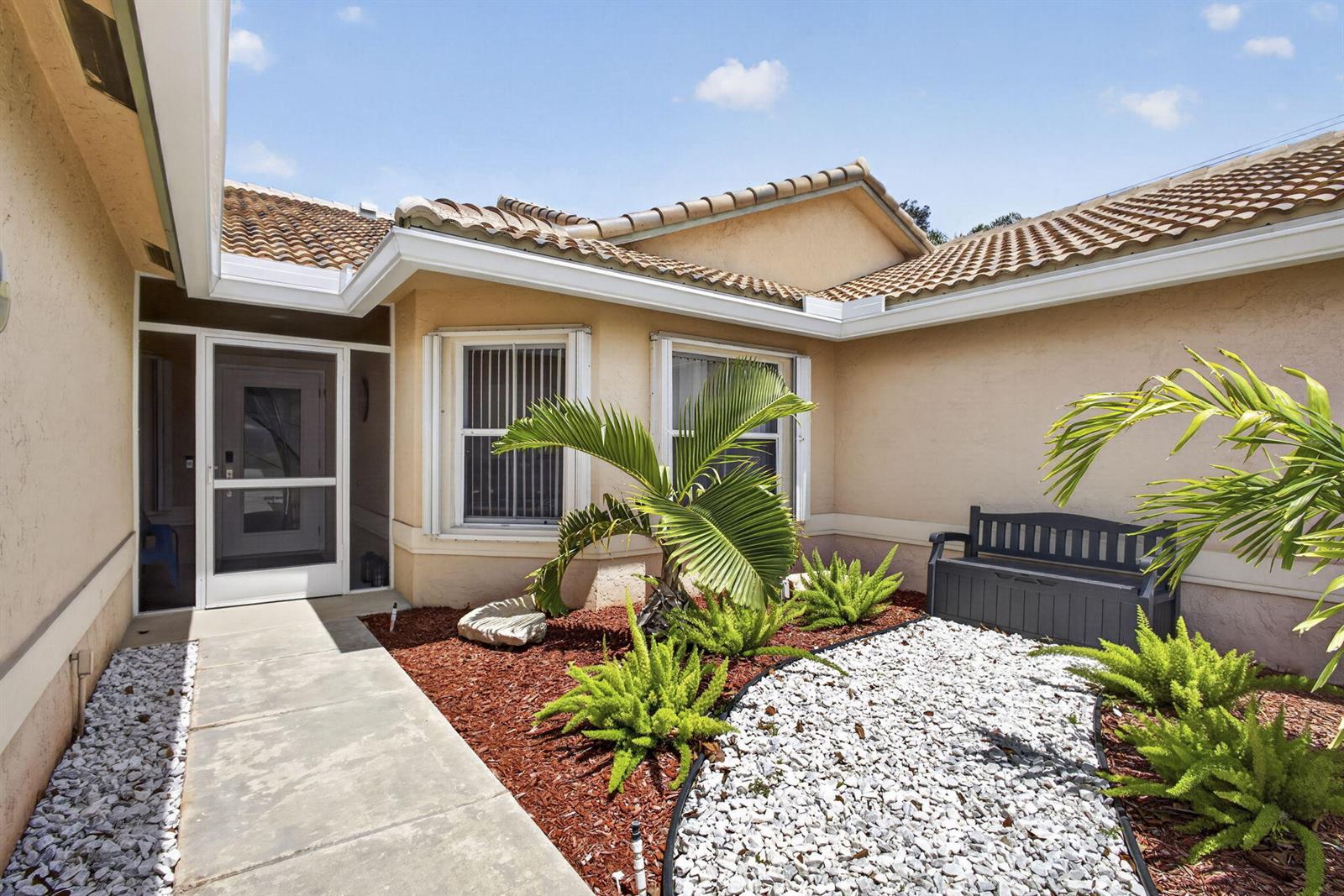 A concrete walkway leads to a front entrance with a screen door and landscaping — 10469 Pelican Drive, Wellington FL 33414, WELLINGTON, FL