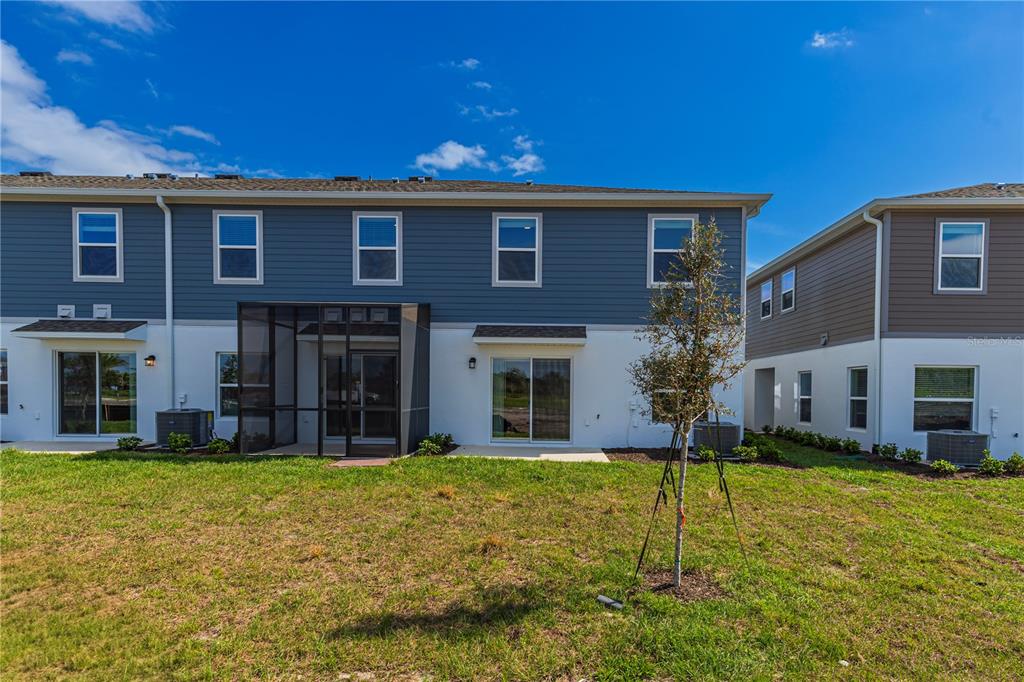 The rear exterior of a two-story townhouse features blue siding, white stucco, and a patio — 5060 RAIN SHADOW DRIVE, ST CLOUD, FL