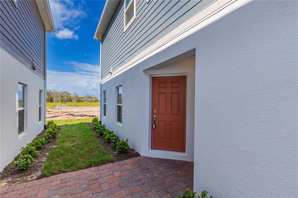 A red door is recessed into the white stucco side wall of a modern house — 5060 RAIN SHADOW DRIVE, ST CLOUD, FL
