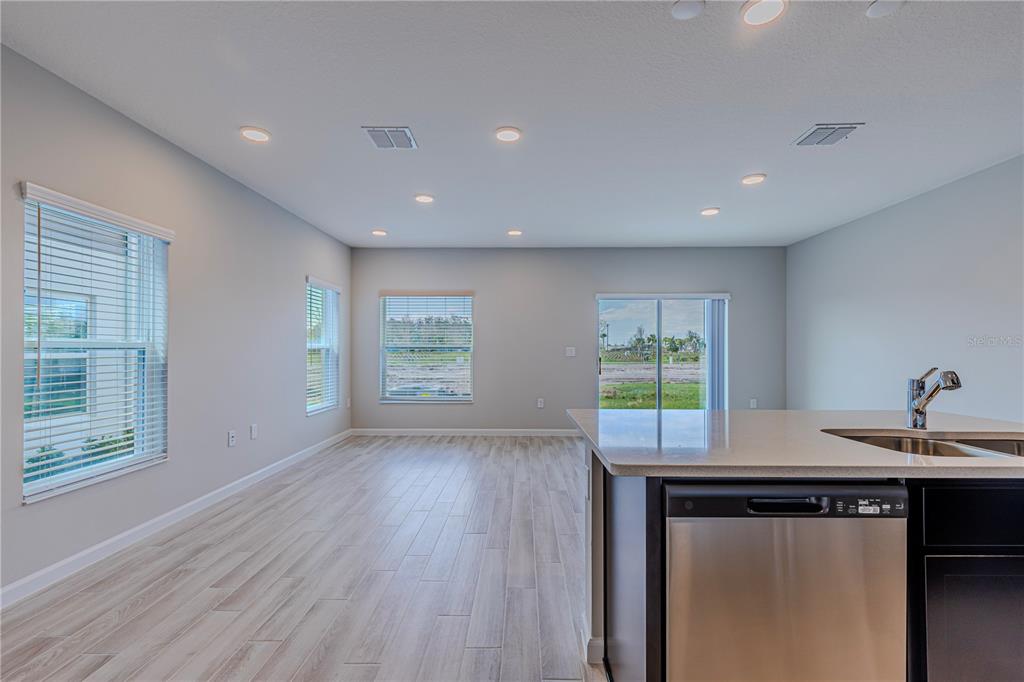 A kitchen island with a stainless steel dishwasher overlooks an open-concept living area with windows — 5060 RAIN SHADOW DRIVE, ST CLOUD, FL