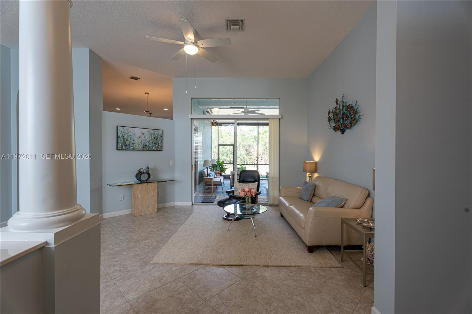A living room features light blue walls, tile flooring, a beige sofa, and glass tables — 6918 SE Sleepy Hollow Ln, Stuart FL 34997, STUART, FL