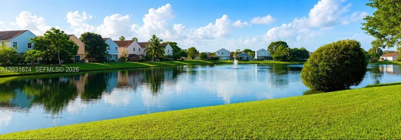 A grassy lawn overlooks a lake with a fountain and houses in the background — MIRAMAR, FL