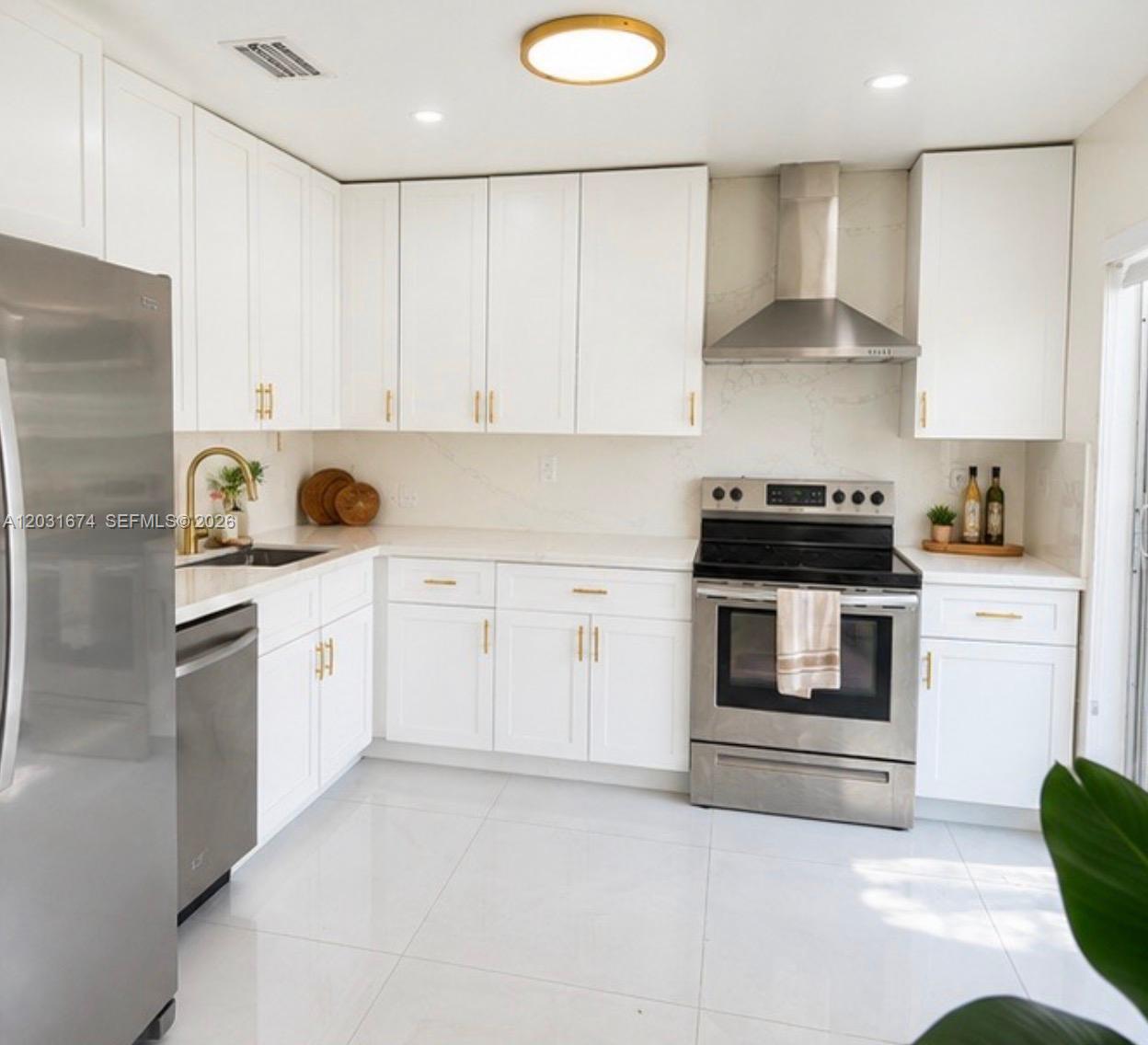 A modern kitchen features white cabinets, stainless steel appliances, gold hardware, and white countertops — MIRAMAR, FL