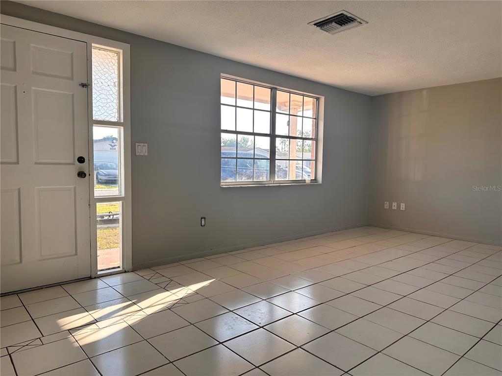 An empty room features white tiled floors, light blue walls, and a front entry door — 3215 BRIGHT DRIVE, HOLIDAY, FL