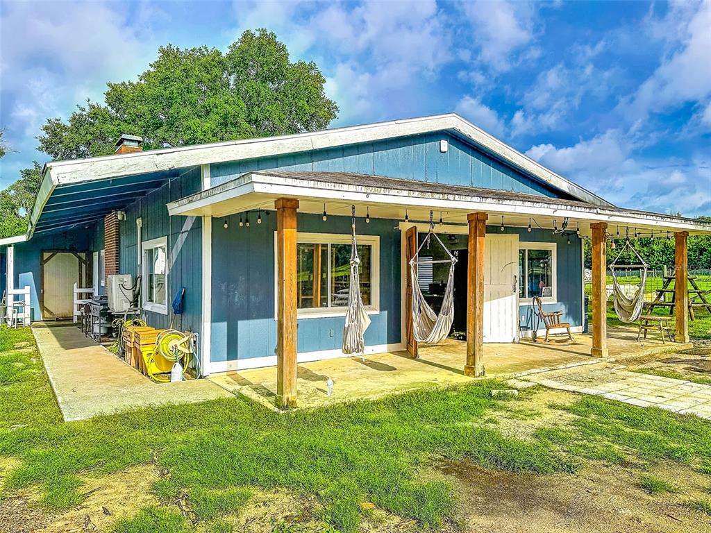 A blue single-story house with a covered porch, wooden posts, and hanging chairs — 16736 POWERLINE ROAD, DADE CITY, FL