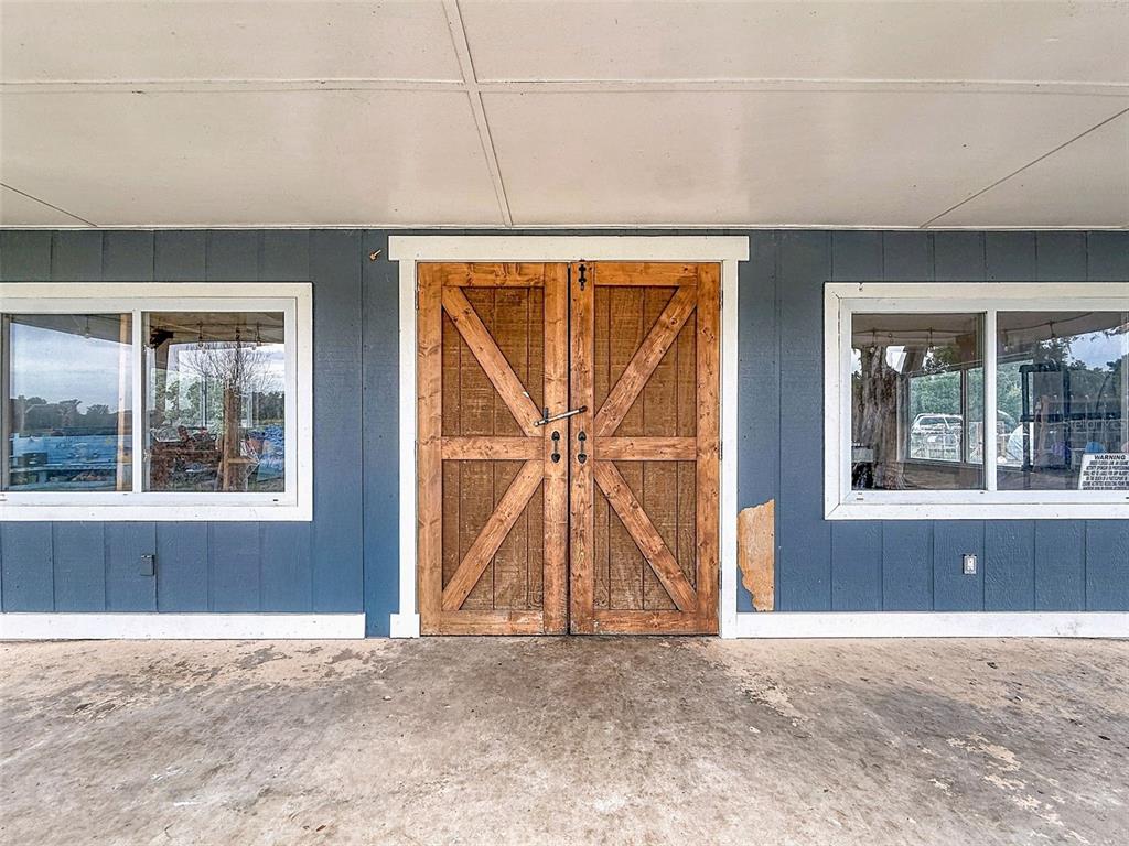A blue exterior wall features a set of wooden barn doors between two windows — 16736 POWERLINE ROAD, DADE CITY, FL