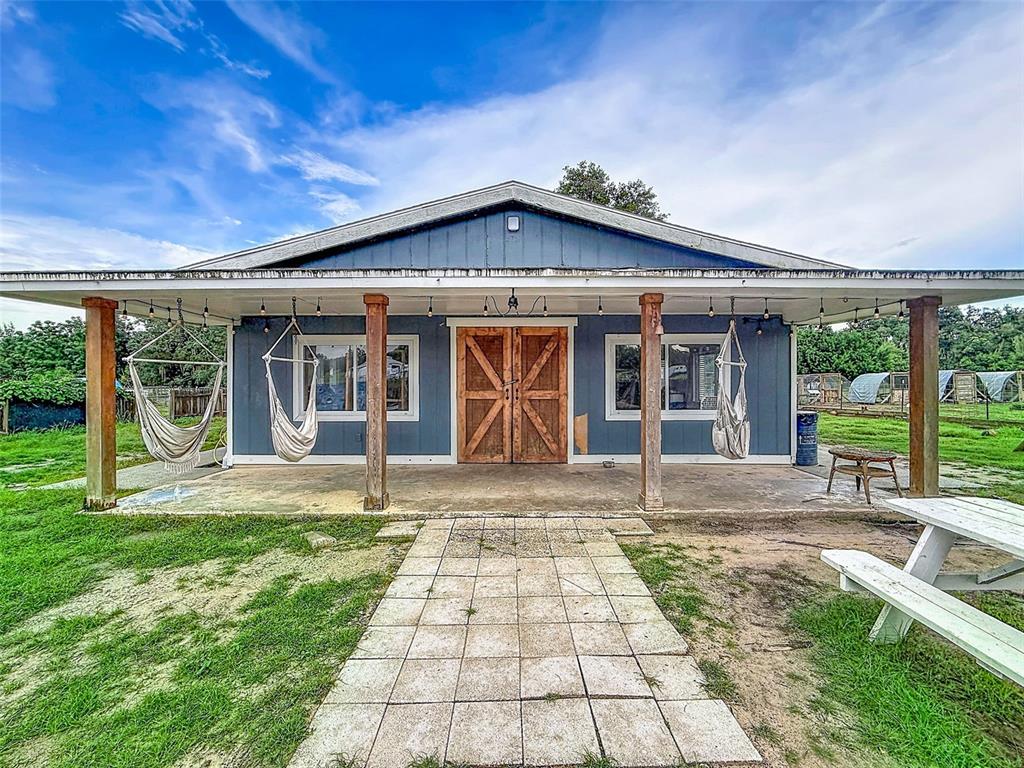 A blue exterior building features a covered porch with two hanging chairs and wooden doors — 16736 POWERLINE ROAD, DADE CITY, FL