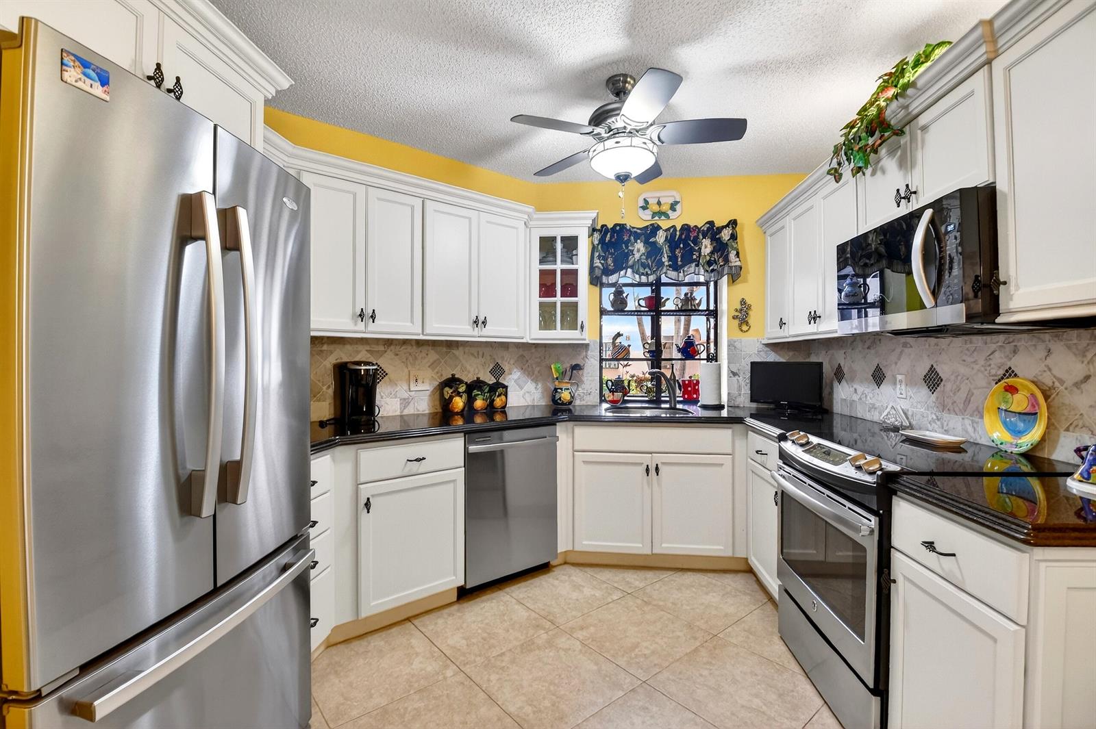 A kitchen features white cabinets, black countertops, stainless steel appliances, and yellow walls — 5188 Europa Drive # G, Boynton Beach FL 33437, BOYNTON BEACH, FL