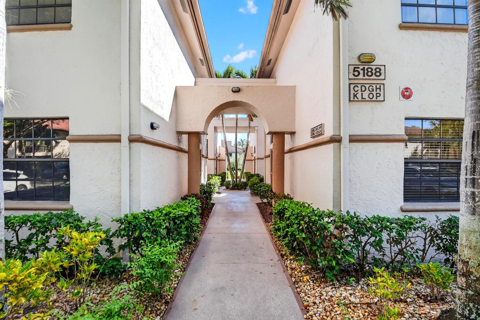 A concrete walkway leads through an arched entryway between two beige apartment building sections — 5188 Europa Drive # G, Boynton Beach FL 33437, BOYNTON BEACH, FL