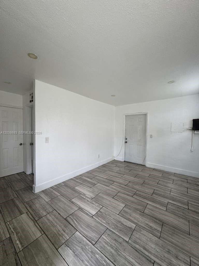 An empty room features white walls, a white door, and grey wood-look tile flooring — FLORIDA CITY, FL