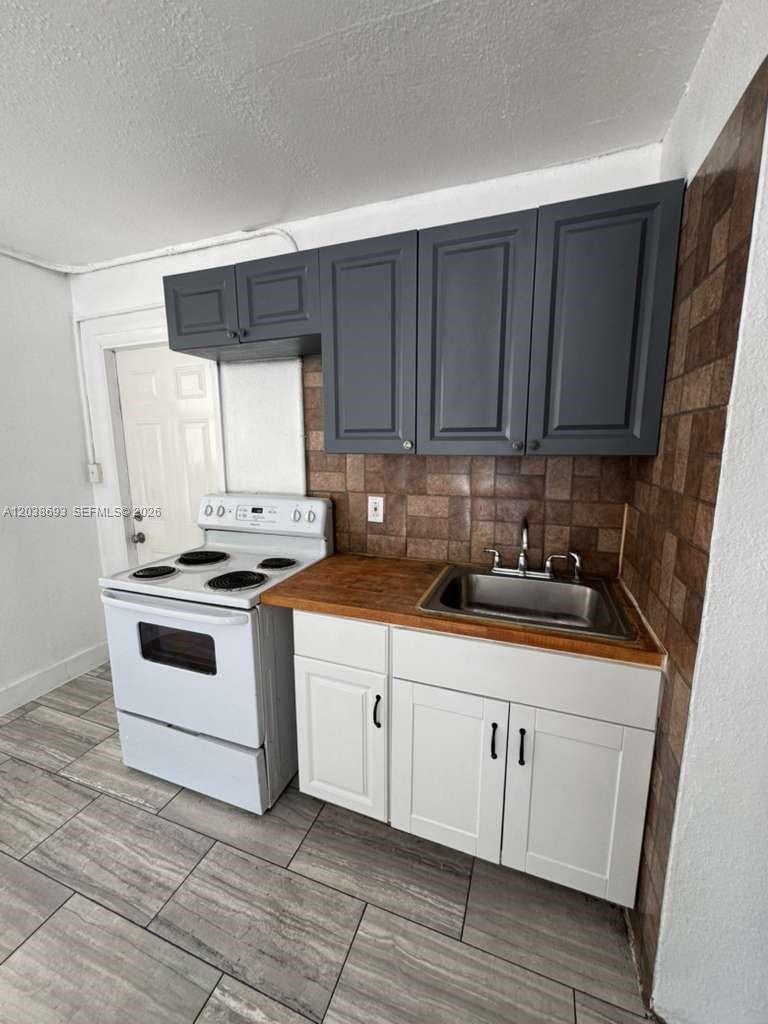 A small kitchen features white lower cabinets, dark gray upper cabinets, and a stainless sink — FLORIDA CITY, FL