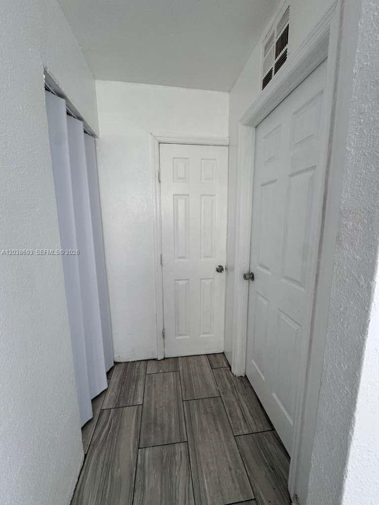 A hallway features white walls, two white doors, and wood-look tile flooring — FLORIDA CITY, FL