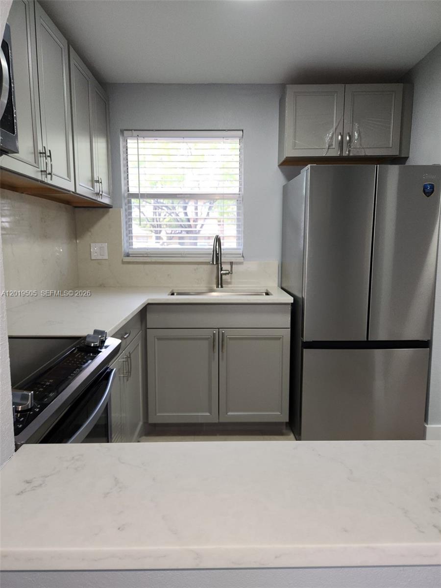 A kitchen features gray cabinets, stainless steel appliances, and white marble-look countertops — 2811 N Pine Island Rd # 107, Sunrise FL 33322, SUNRISE, FL