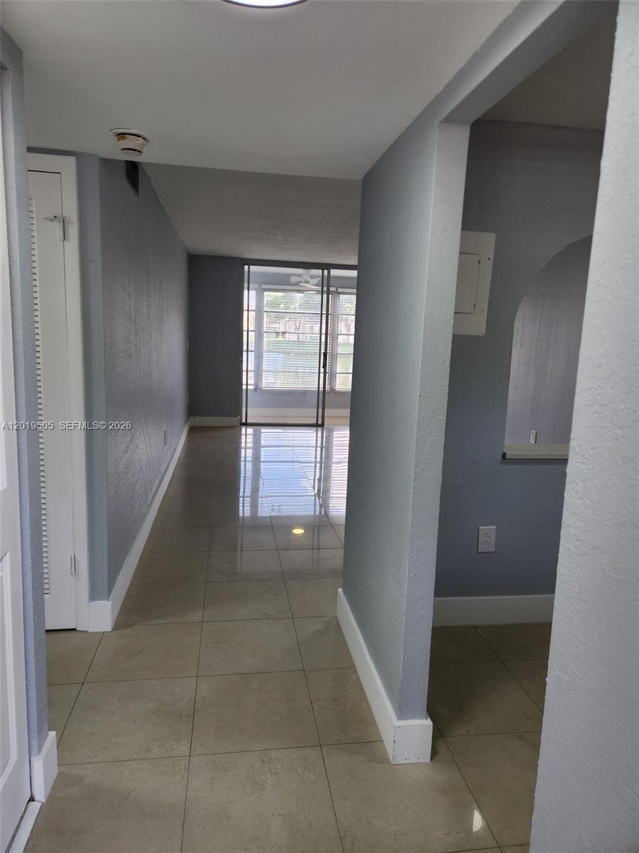 A hallway with light-colored tile flooring leads toward a glass sliding door overlooking a lake — 2811 N Pine Island Rd # 107, Sunrise FL 33322, SUNRISE, FL