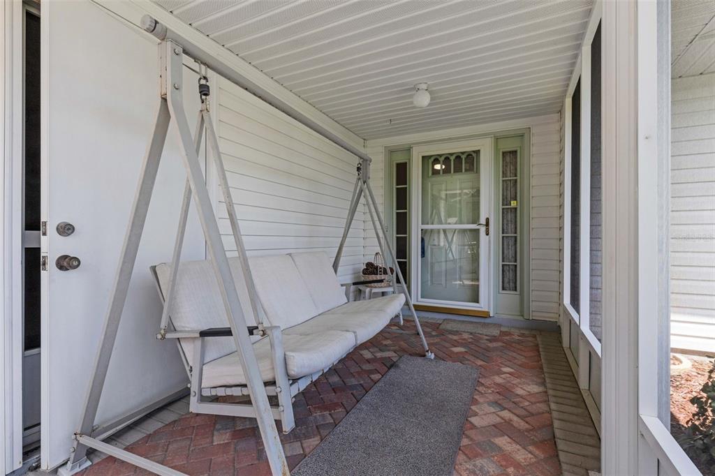 A covered porch features a white metal swing, brick flooring, and a screened-in entry door — 6033 WADE STREET, LEESBURG, FL