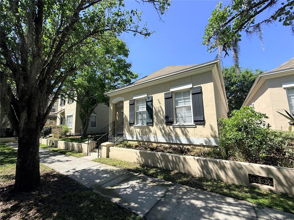 A tan single-story house with dark shutters sits behind a low concrete wall and sidewalk — 1107 CROTON PLACE, CELEBRATION, FL