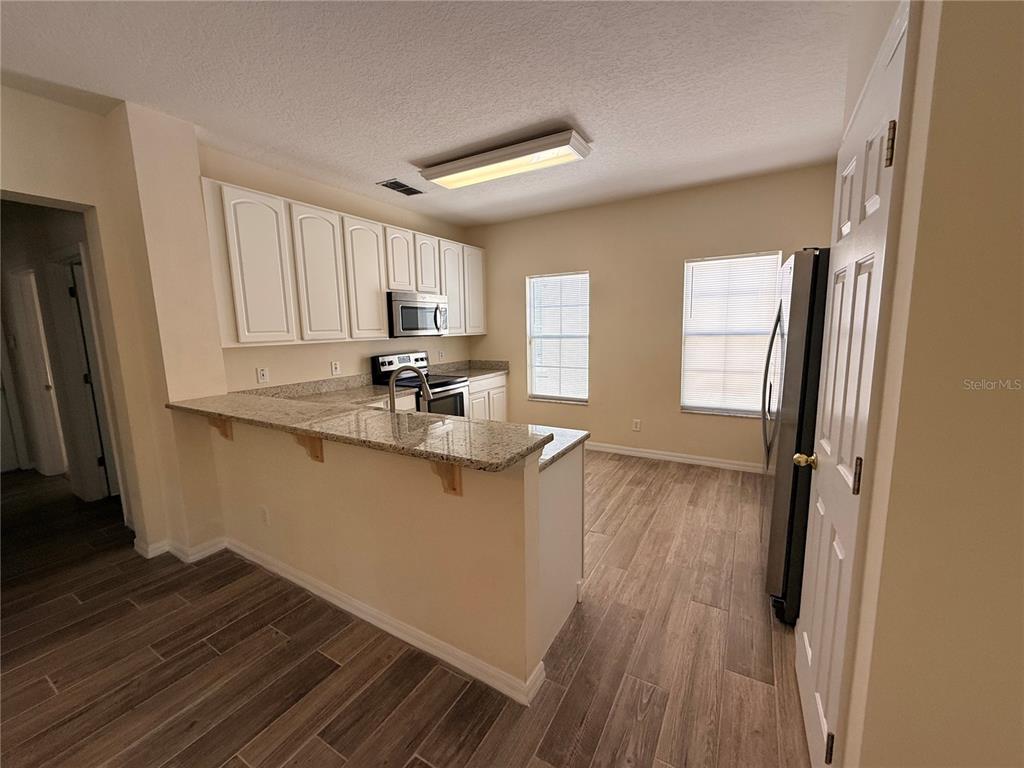 A kitchen features white cabinets, granite countertops, a breakfast bar, and wood-look tile flooring — 1107 CROTON PLACE, CELEBRATION, FL