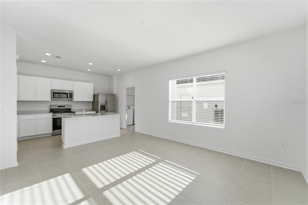 A bright, open-concept kitchen and living area with white cabinets, stainless appliances, and tile flooring — 2196 RED SUN STREET, APOPKA, FL