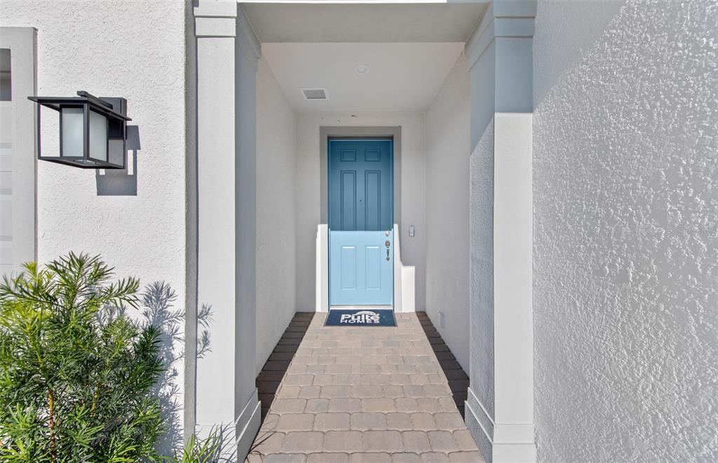 A blue front door is centered at the end of a paved entryway walkway — 1758 PEPPER GRASS DRIVE, NORTH PORT, FL