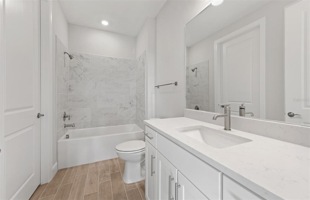 A bathroom features a white vanity with a quartz countertop, a toilet, and a tiled tub — 1758 PEPPER GRASS DRIVE, NORTH PORT, FL