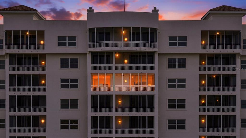 The exterior of a multi-story apartment building features screened balconies and glowing interior lights at dusk — 2925 TERRA CEIA BAY BOULEVARD UNIT 2703, PALMETTO, FL