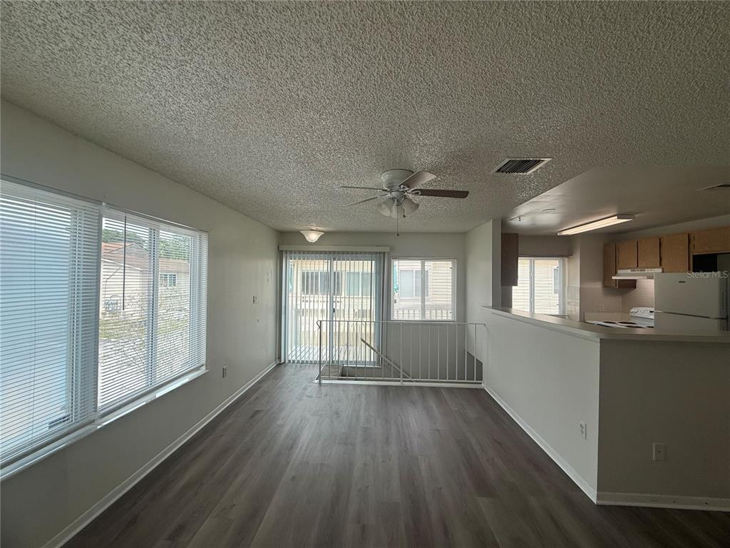 An open-concept living area features wood-look flooring, a ceiling fan, and a kitchen pass-through — 1101 SPRING MEADOW DRIVE UNIT 1101, KISSIMMEE, FL