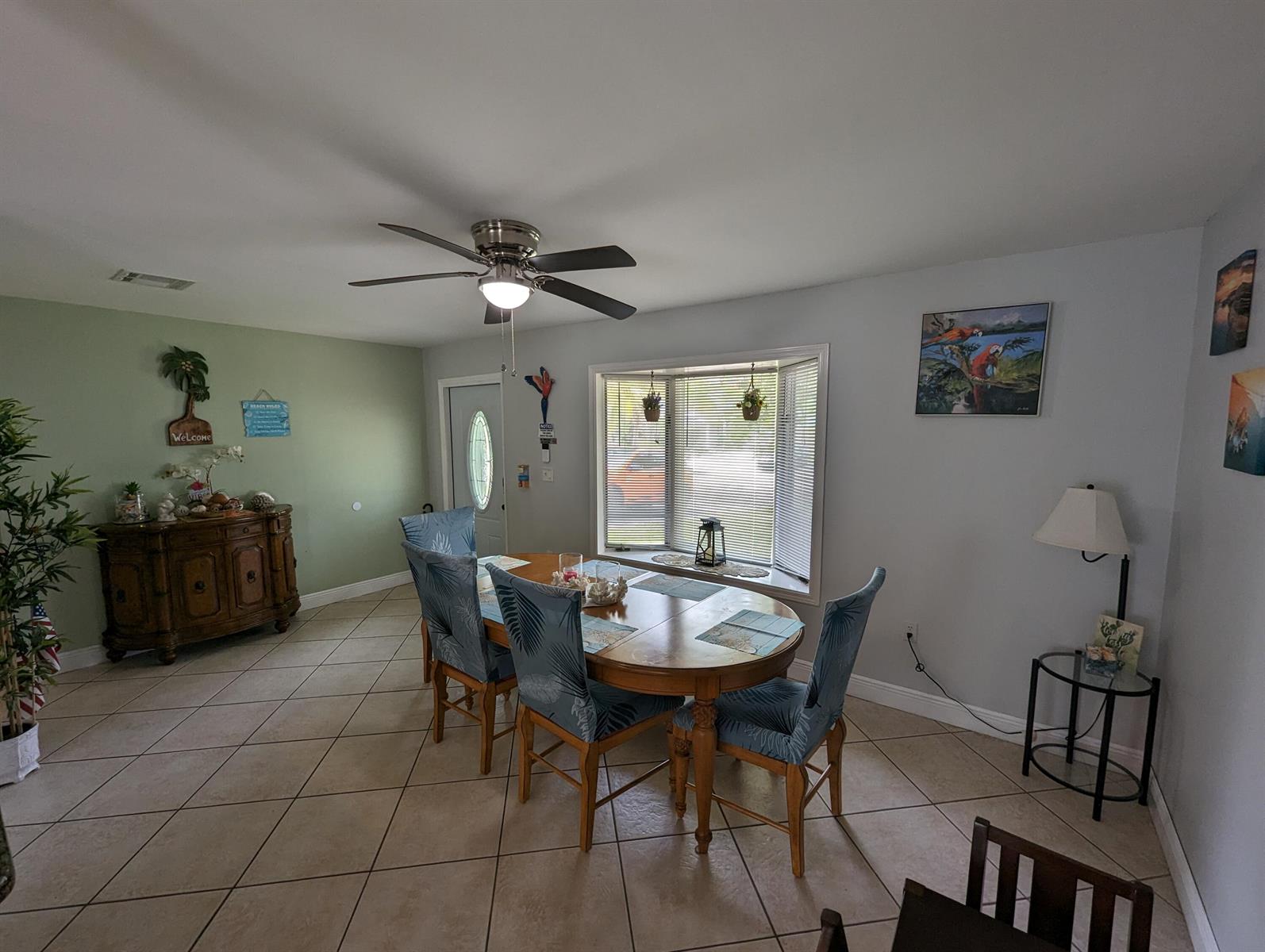 A dining room features a wooden table with blue chairs, tile flooring, and a bay window — 2394 Zeder Avenue, Delray Beach FL 33444, DELRAY BEACH, FL