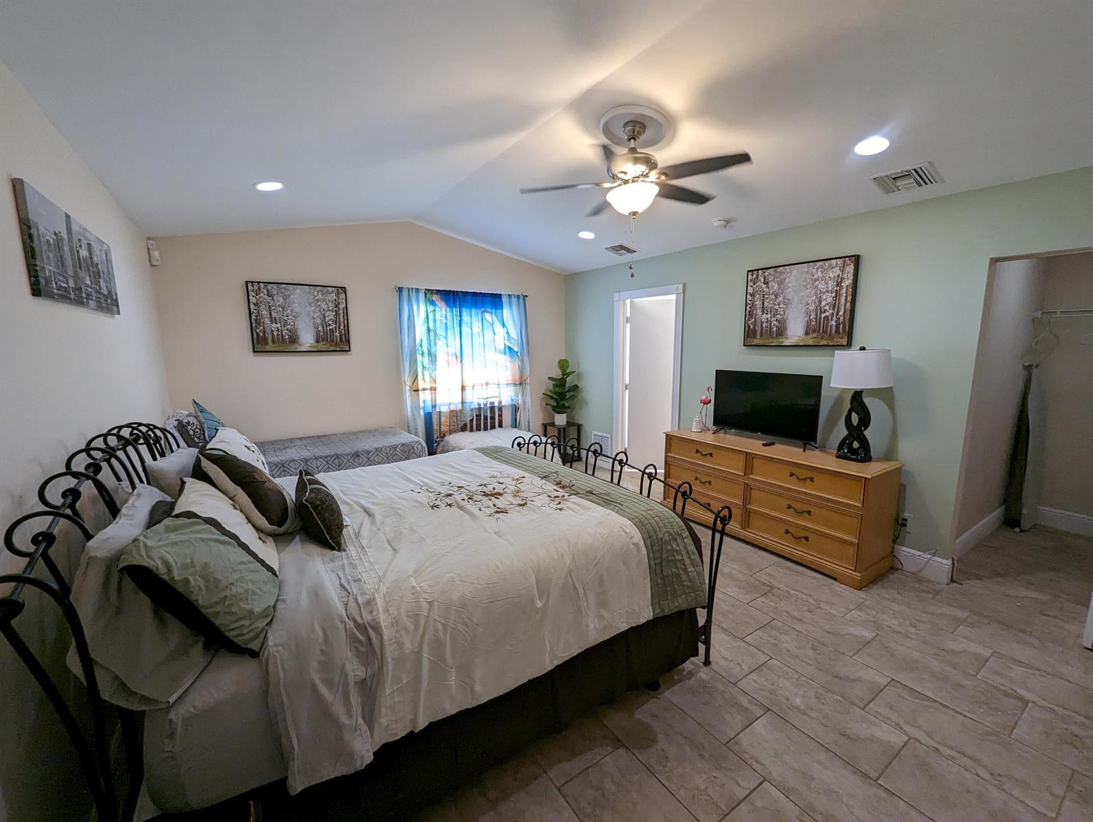 A bedroom features a wrought-iron bed, a wooden dresser with a television, and tile flooring — 2394 Zeder Avenue, Delray Beach FL 33444, DELRAY BEACH, FL