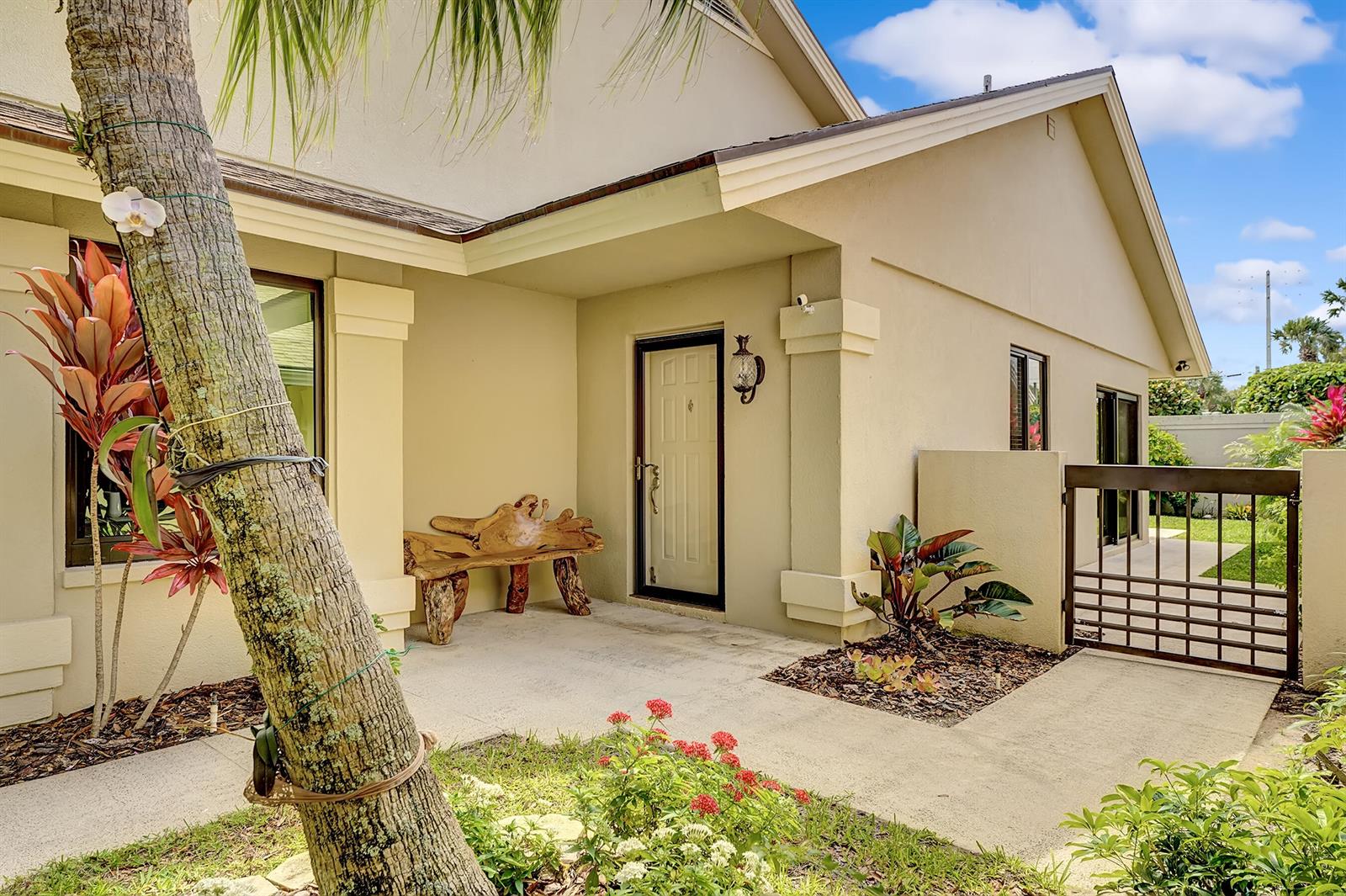 A beige house exterior features a covered entryway, a wooden bench, and a metal gate — 118 Ridge Road, Jupiter FL 33477, JUPITER, FL